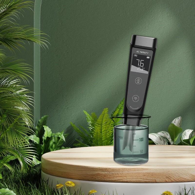 Professional hydroponic pH meter with digital display and interchangeable probe testing solution in beaker, displayed on wooden platform with decorative plants and green background.