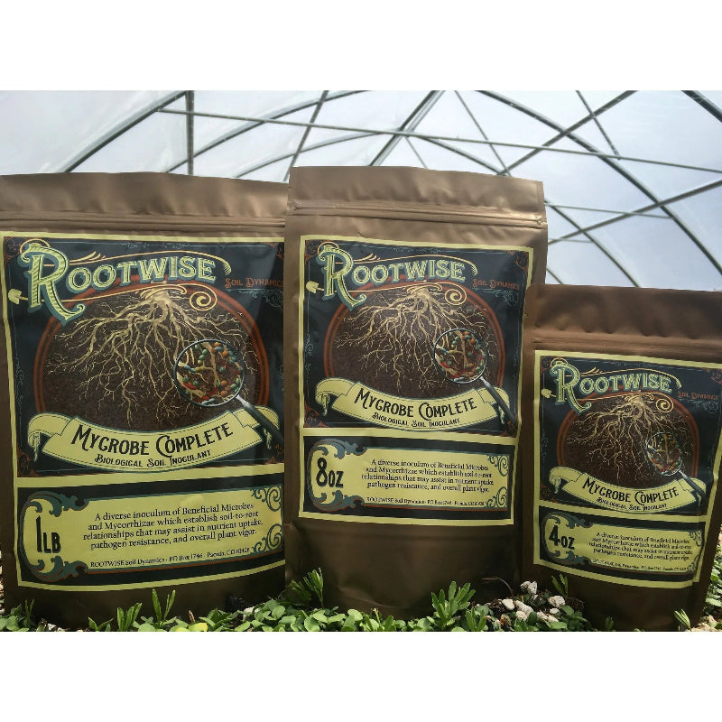 Rootwise Mycrobe Complete microbial inoculant in three sizes - 1lb, 8oz, and 4oz resealable pouches shown in greenhouse setting with detailed root system artwork.