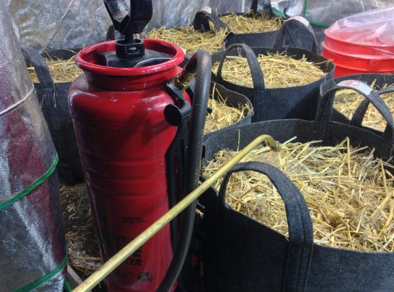 BuildASoil Organic Straw Mulch with red pump sprayer and fabric grow pots - professional garden setup showing natural mulch application.